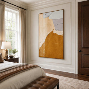 Wood framed ochre and beige abstract artwork beside a bed with warm brown linens.