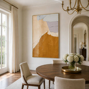 Gold framed ochre abstract artwork beside a round dining table with white hydrangeas.