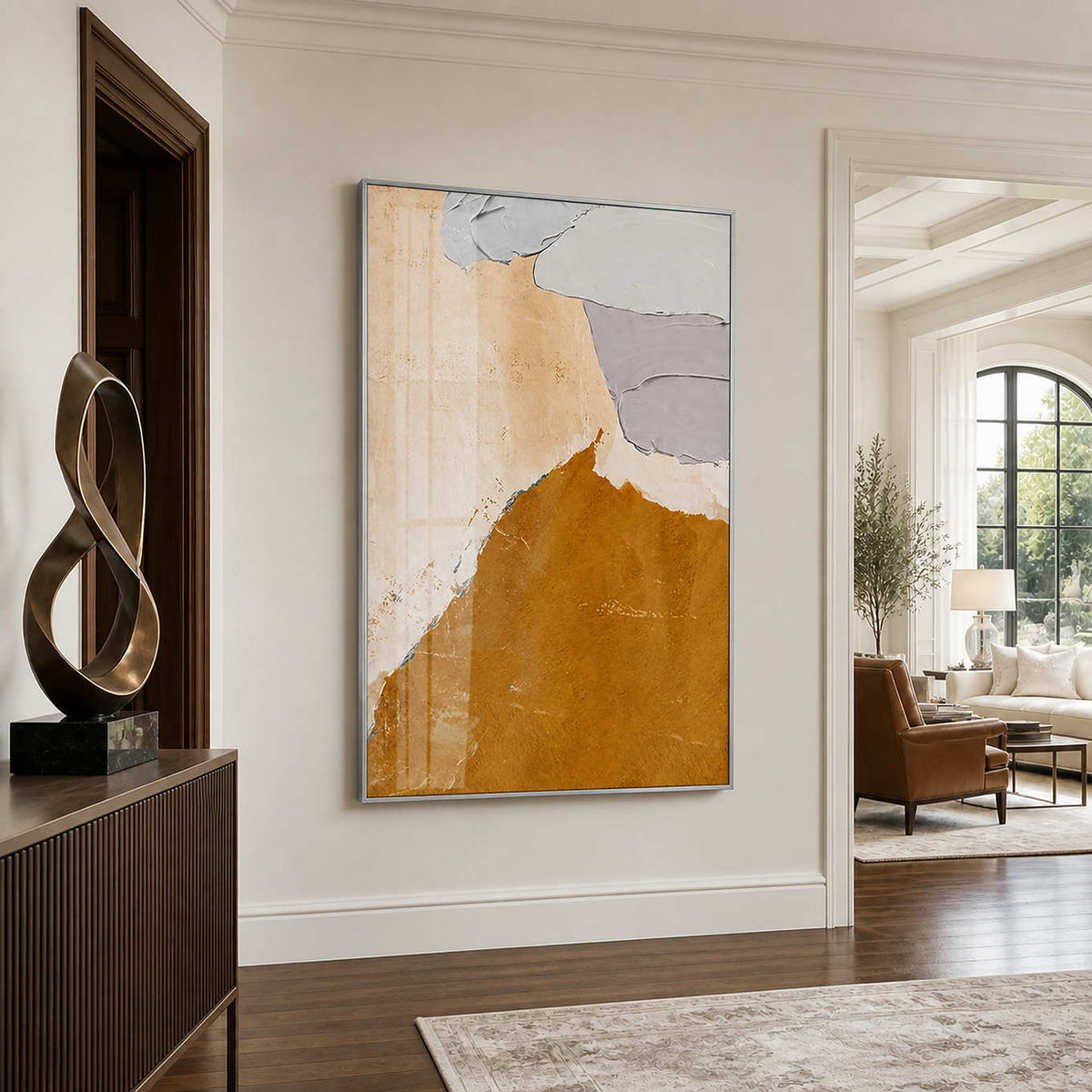 Silver framed warm abstract artwork beside a sculptural bronze ornament in a residential entryway.