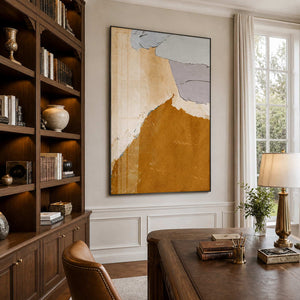 Black framed ochre abstract artwork beside wooden bookshelves and a traditional home office desk.