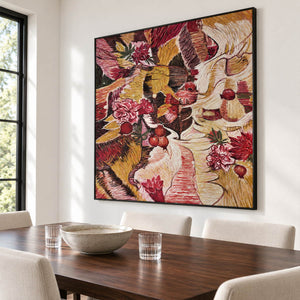 Artwork showing red flowers and rounded fruit forms woven through ochre, cream and dark bands in a dining area beside the table, with a black frame.