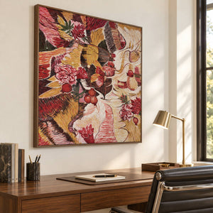 In a study with a desk, an artwork with a brown wood-look frame shows red flowers and rounded fruit forms woven through ochre, cream and dark bands.