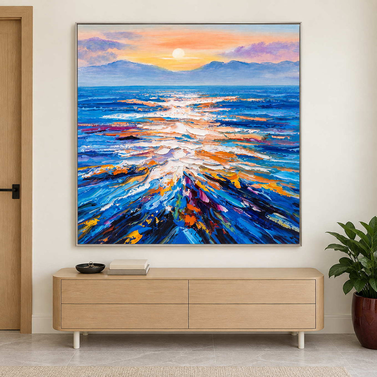 Square sea reflection painting above a low pale wood cabinet near a potted plant.