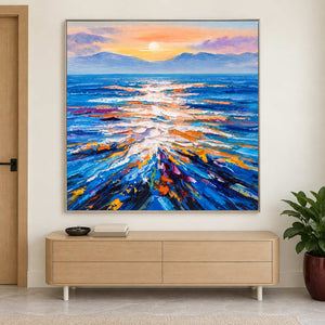 Square sea reflection painting above a low pale wood cabinet near a potted plant.