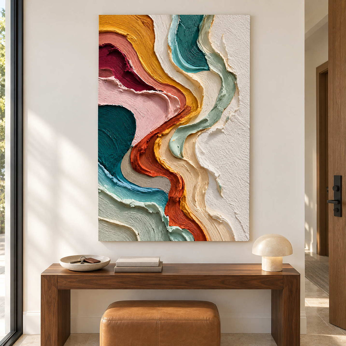 Vertical color artwork above a wooden console with a tan ottoman.