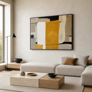 Black framed ochre abstract painting above a cream sofa in a sunlit living room.