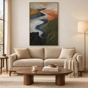 A winding pale waterway between dark green and rust-colored fields in a gold frame, displayed above a sofa in a living room.