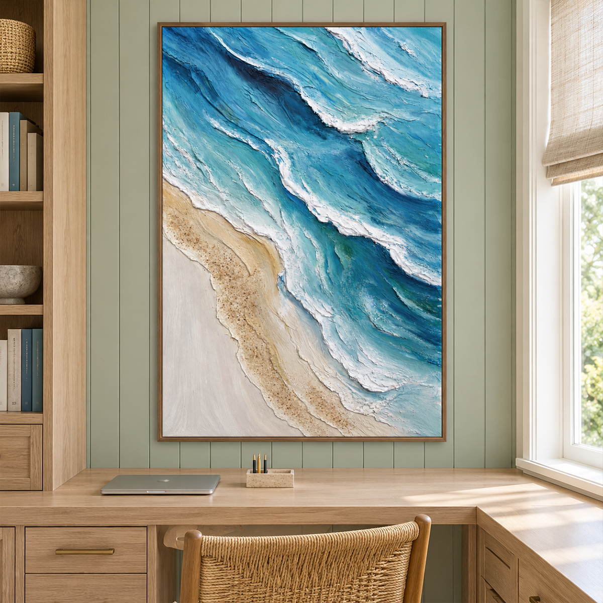 Layered blue-green waves with raised white edges beside a pale sandy shore in an artwork with a brown wood-look frame, displayed in a study with a desk.
