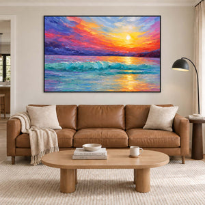 A golden sunset above turquoise waves and a purple-red sky in a black frame, displayed above a sofa in a living room.