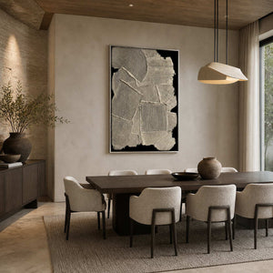 Silver framed cream and black relief artwork behind a dark dining table and upholstered chairs.