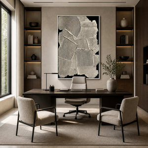 White framed black and cream abstract artwork behind an office desk between illuminated shelves.