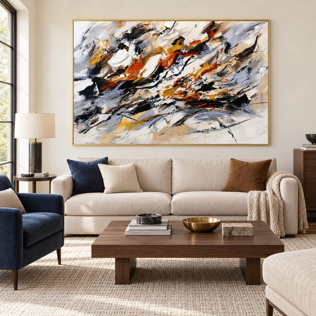 Hand-painted abstract artwork with black gestures and rust, ochre, ivory, and gray layers, displayed in a living room in a gold frame.