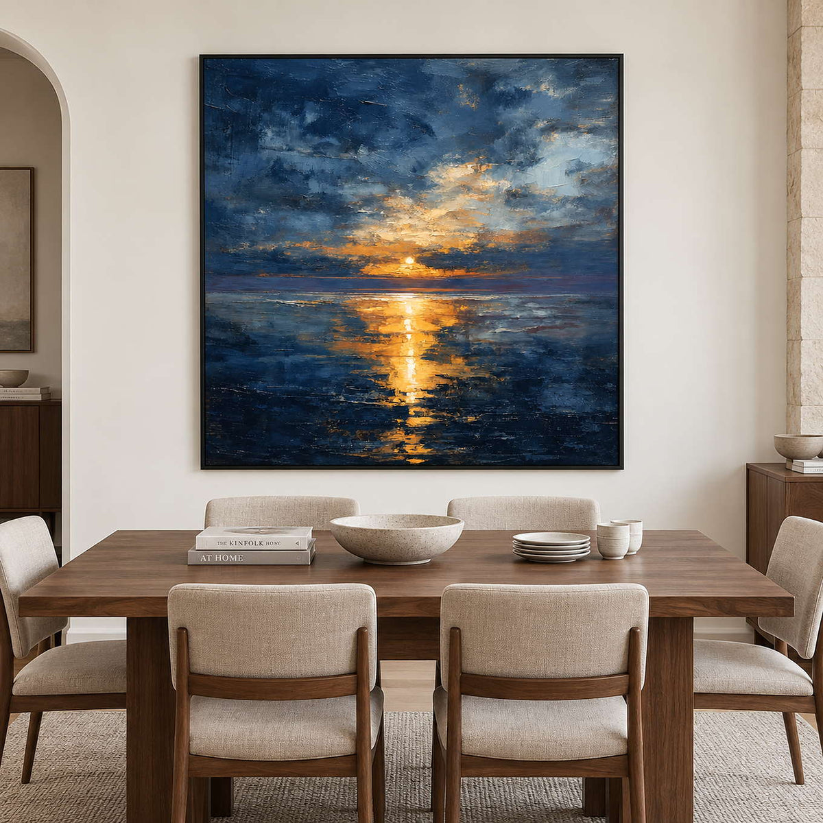 Square sea and sunlight painting above a wood dining table with pale upholstered chairs.
