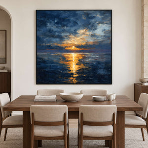 Square sea and sunlight painting above a wood dining table with pale upholstered chairs.
