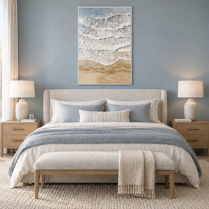 Whispering Tides in a white frame above a neutral bed with blue-gray linens and an upholstered bench.