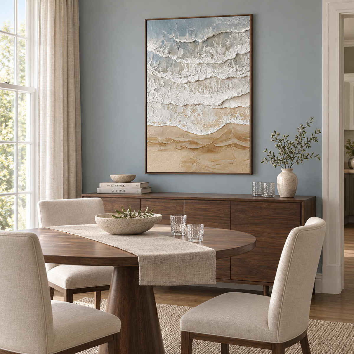 Whispering Tides in a wood frame above a sideboard behind a round dining table against a blue-gray wall.