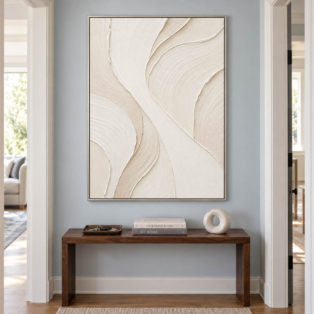 Hand-painted ivory abstract wall art with flowing cream relief and fine combed texture, displayed in a hallway in a silver frame.