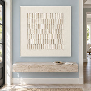Square ivory relief artwork formed by rows of raised vertical marks, displayed in an entrance hall in a white frame.