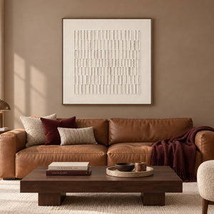 Square ivory relief artwork formed by rows of raised vertical marks, displayed in a living room in a brown wood frame.