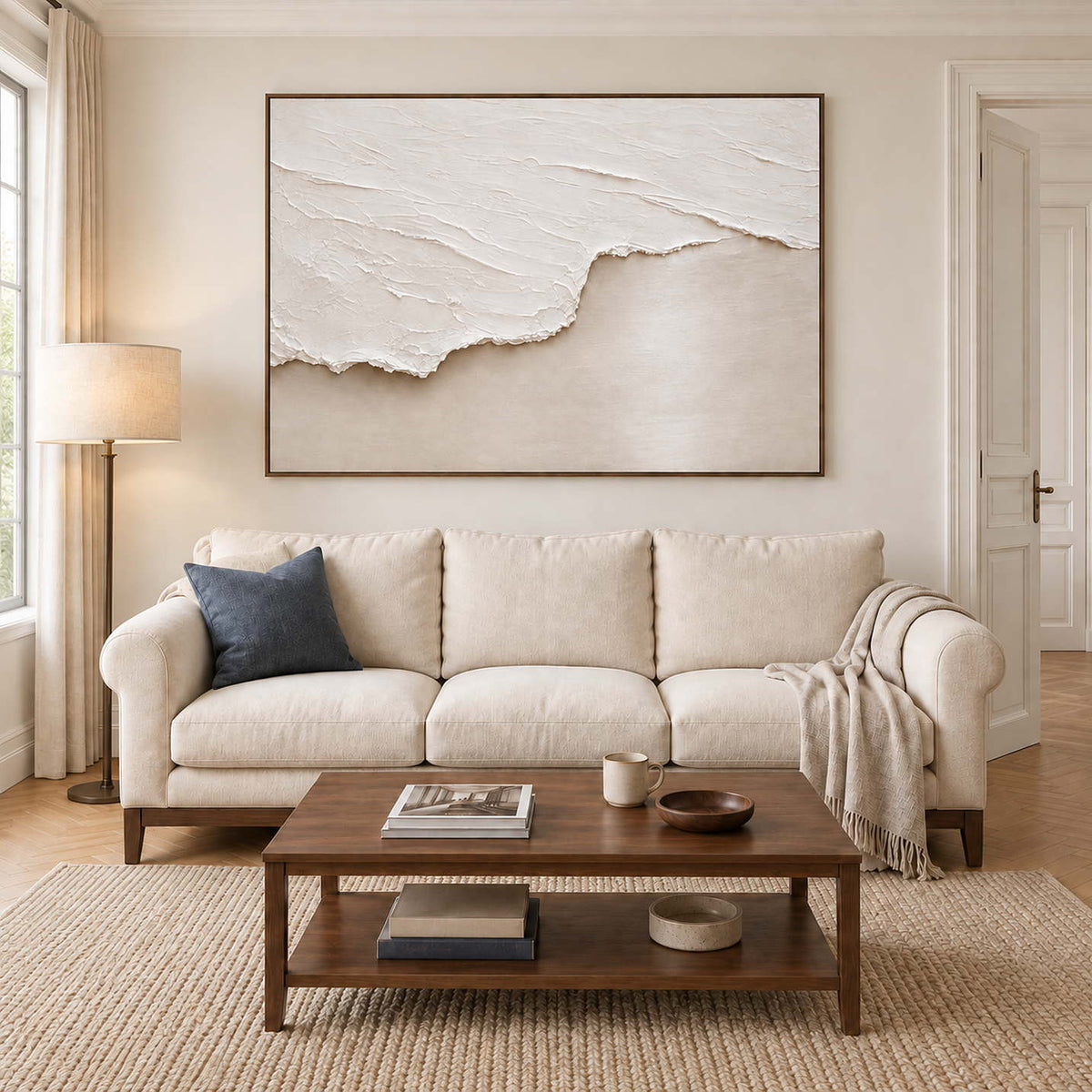 A raised white wave spreading across pale beige sand in a brown wood frame, displayed above a sofa in a living room.