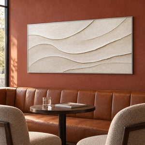 Layered ivory and warm beige relief flowing in quiet panoramic waves, displayed in a lounge in a silver frame.