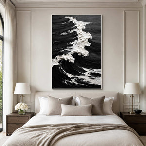 White framed coastal painting with a textured white crest above a pale bedroom headboard.
