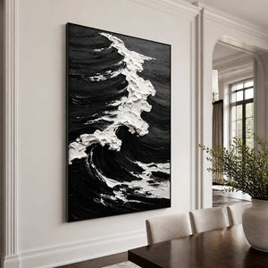 Black framed monochrome wave artwork with white foam beside a wooden dining table.