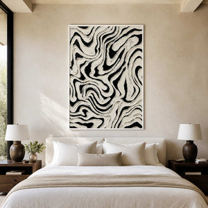 White framed black and white abstract painting with fluid lines above a bedroom headboard.