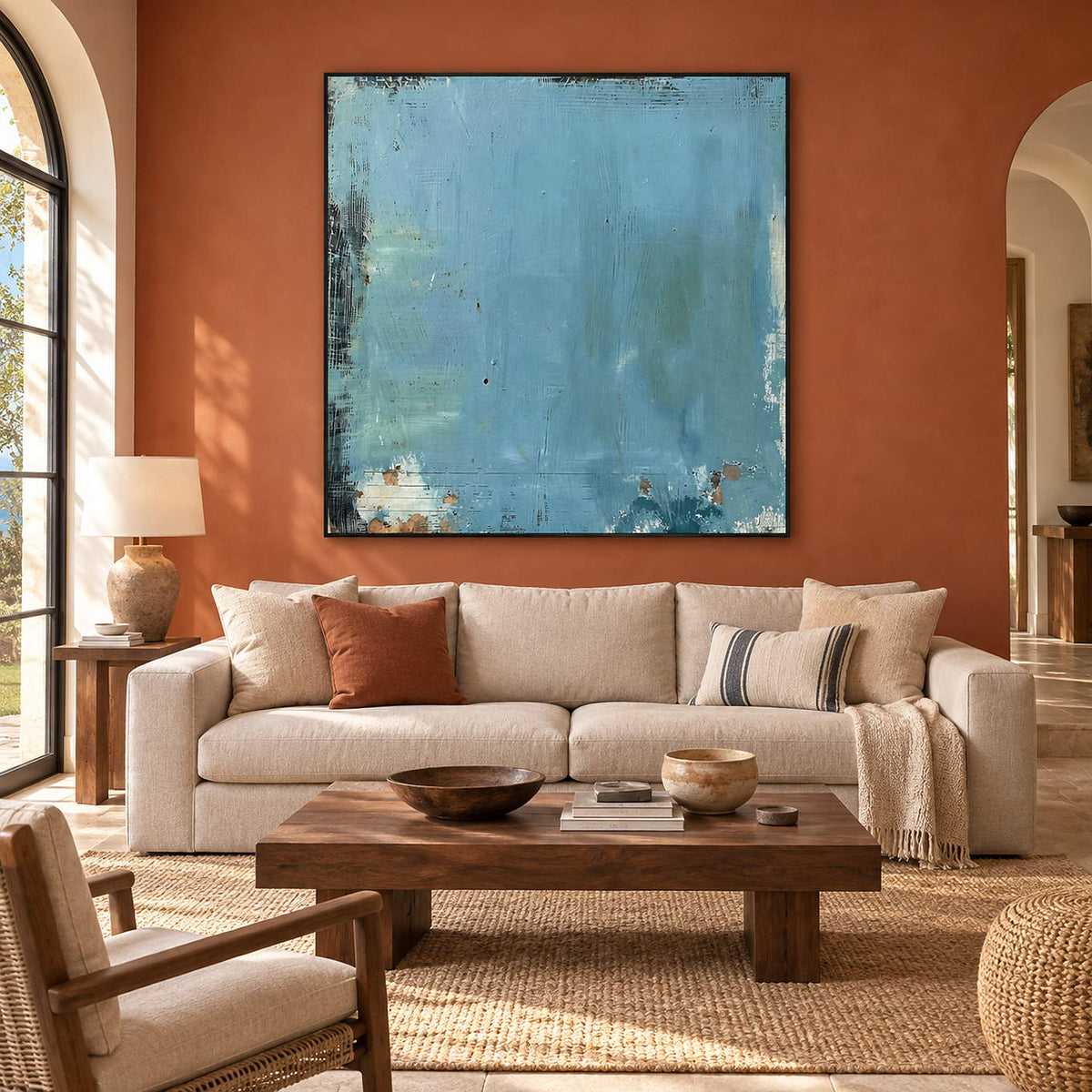 Hand-painted square aqua canvas with weathered dark edges and rust traces, displayed in a living room in a black frame.